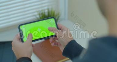 年轻人手里拿着智能<strong>手机</strong>，<strong>玩手机</strong>游戏。 带有彩色钥匙绿色屏幕的移动电话。